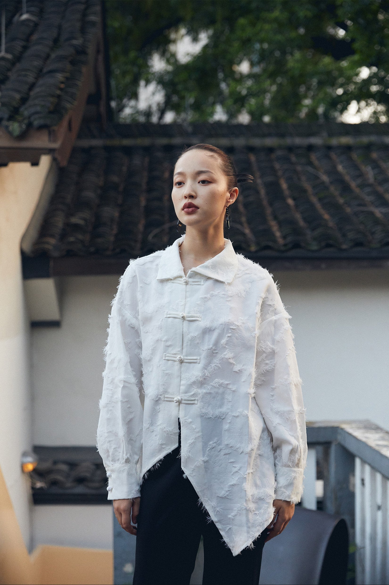 Person wearing a light-colored shirt standing outdoors with traditional architecture in the background