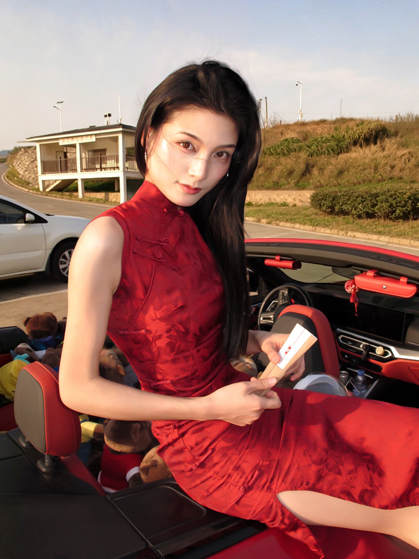 Woman in a red dress sitting in an open car with a scenic background