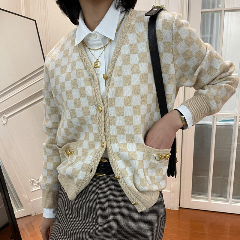 Person wearing a checkered beige and white cardigan with a white shirt and plaid skirt indoors.