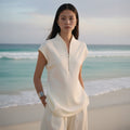 Woman in a white outfit standing on a beach with ocean in the background