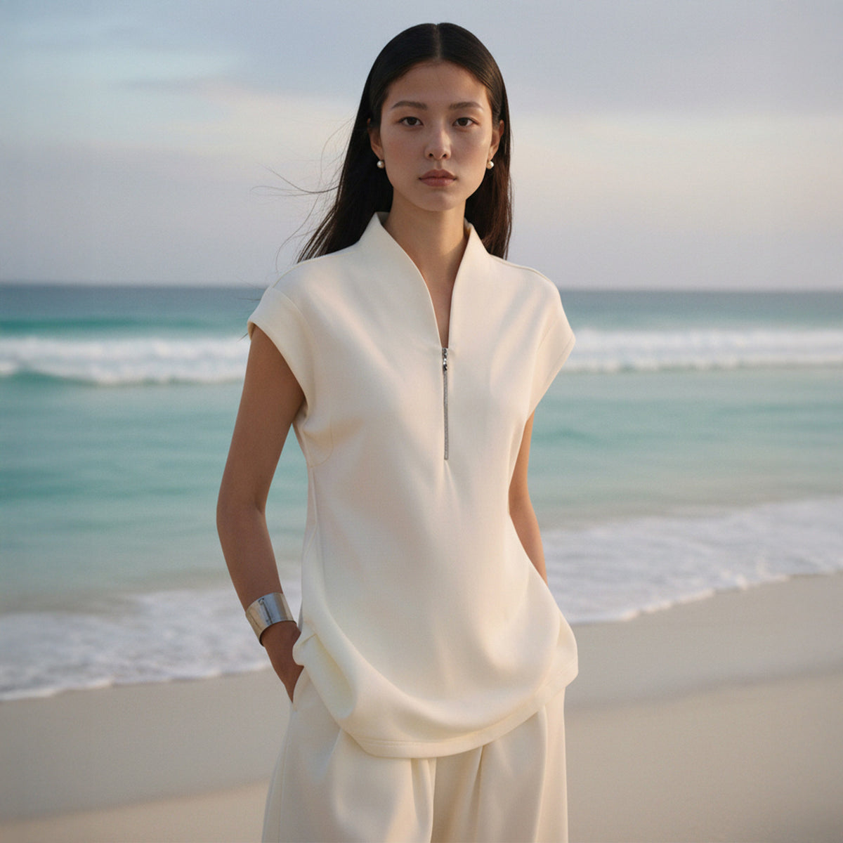 Woman in a white outfit standing on a beach with ocean in the background