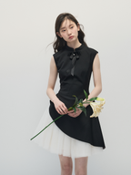 Woman wearing a black sleeveless top with a bow and white skirt holding flowers against a plain background