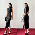 Woman in a black dress with a high slit standing on a red carpet against a white wall.