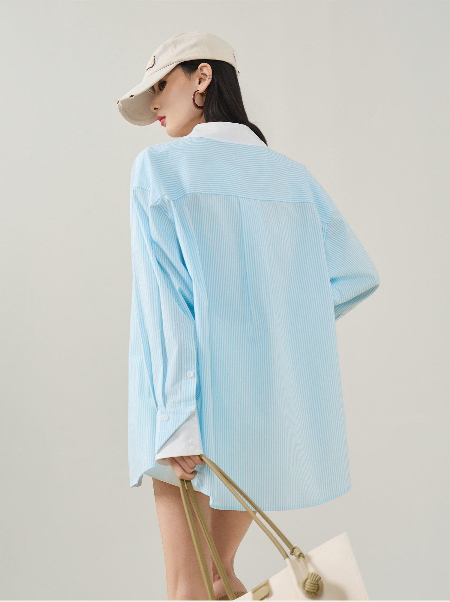 Person wearing a light blue shirt and beige cap on a plain background