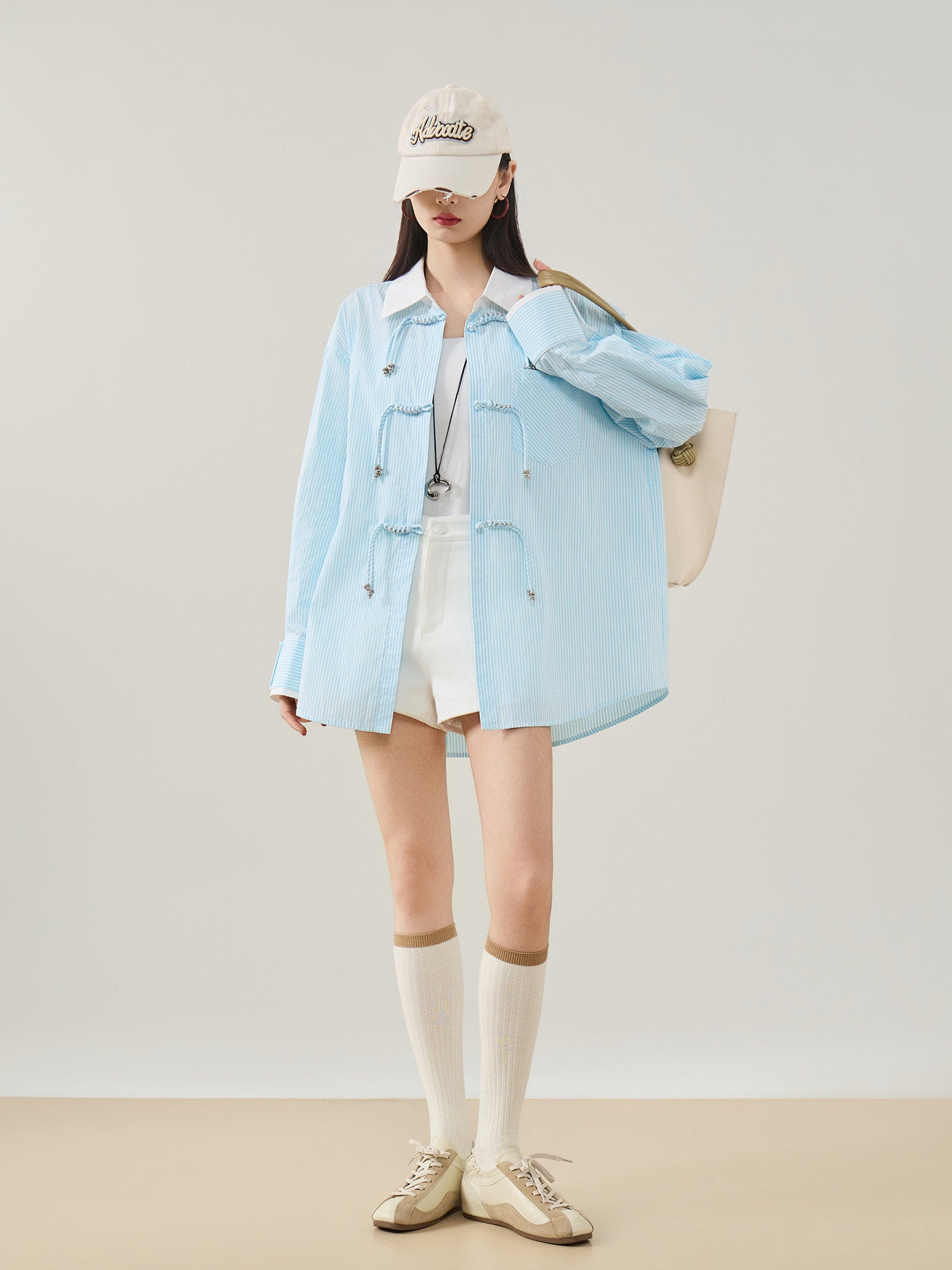 Person wearing a light blue denim jacket, white shorts, and beige sneakers on a plain background