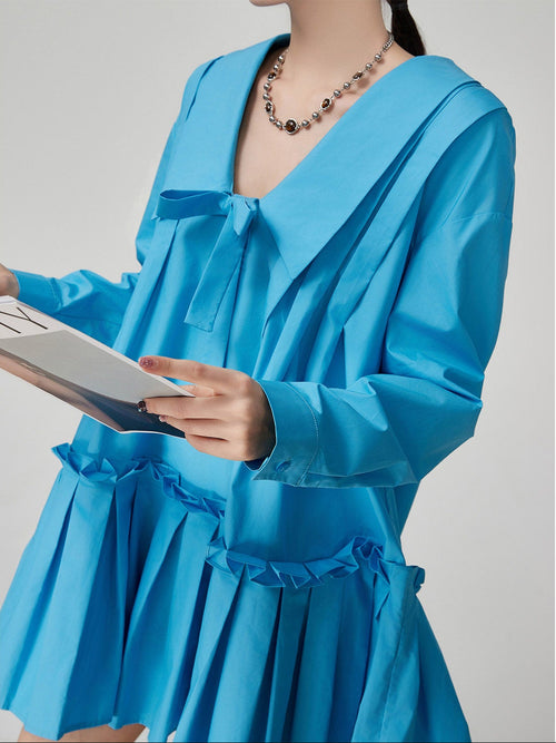 Person wearing a blue dress holding a book against a plain background