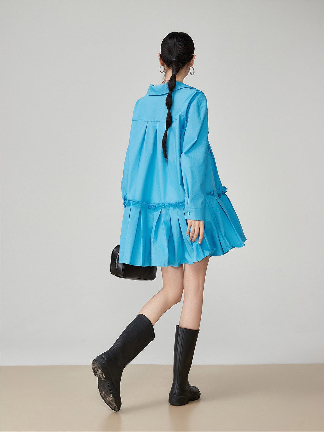Person wearing a blue dress and black rain boots on a plain background