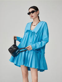 Woman wearing a blue dress holding a black handbag against a gray background