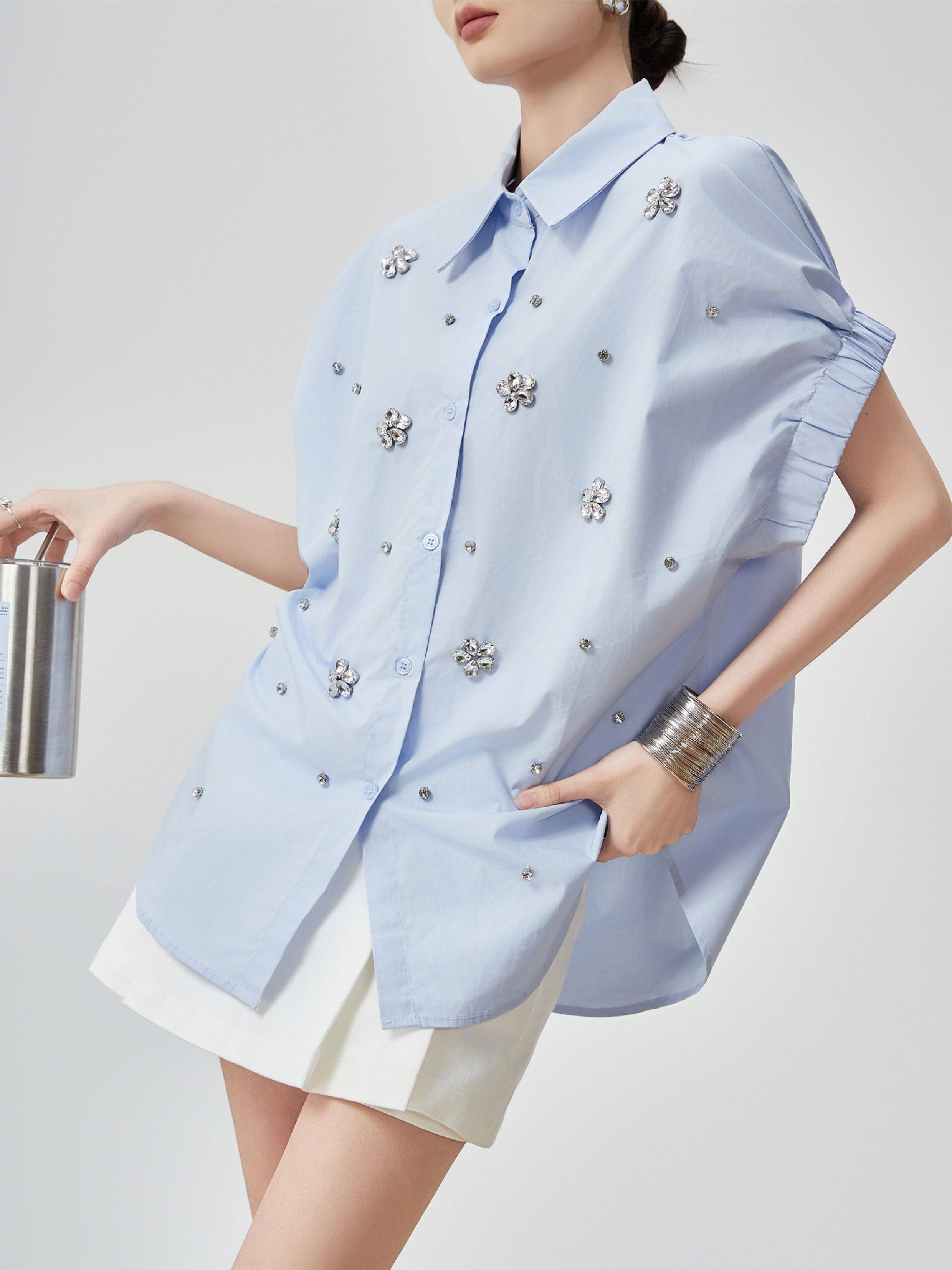 Light blue sleeveless blouse with floral embellishments worn by a person on a plain background