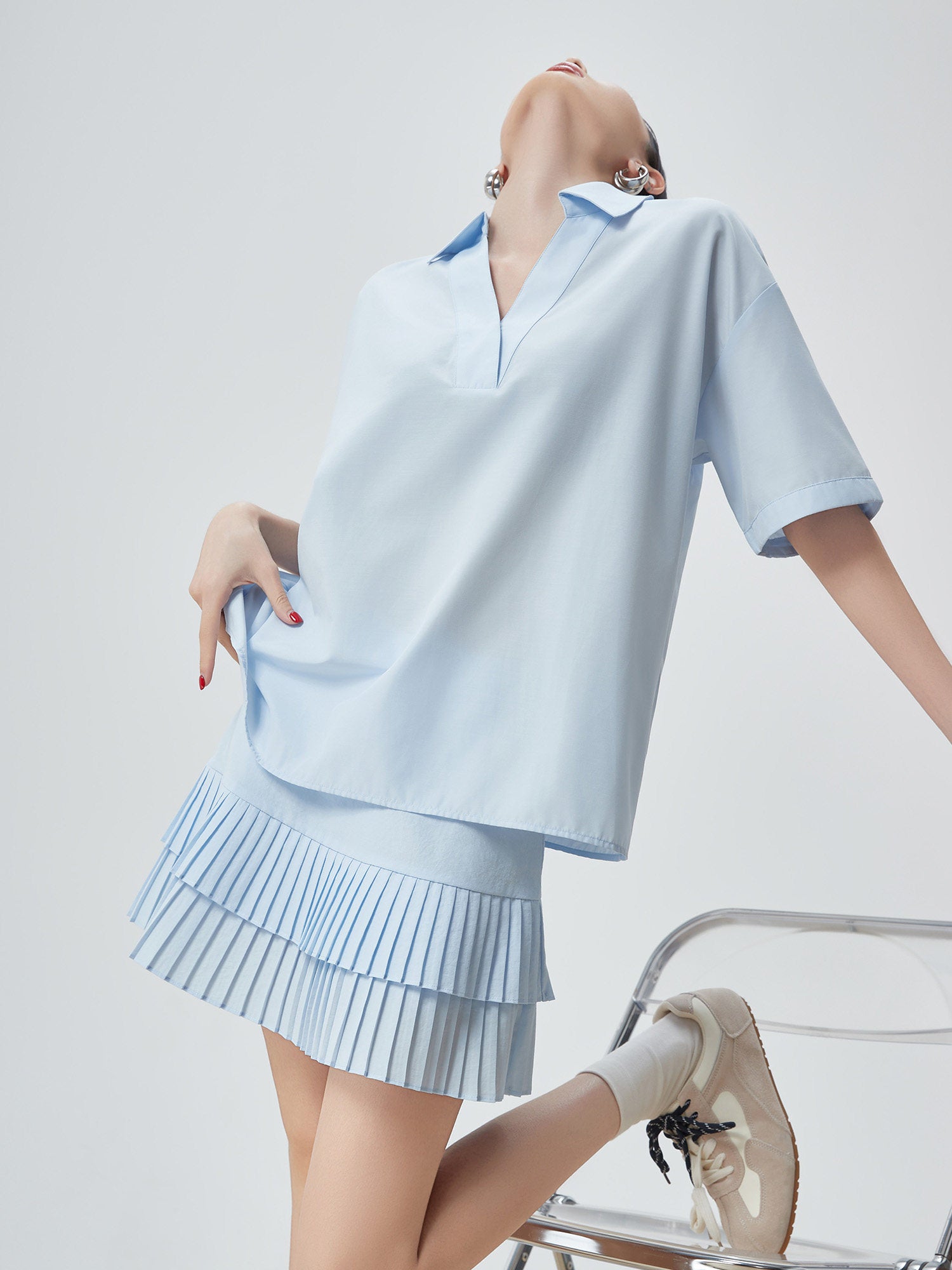 Woman wearing a light blue outfit with a pleated skirt on a plain background