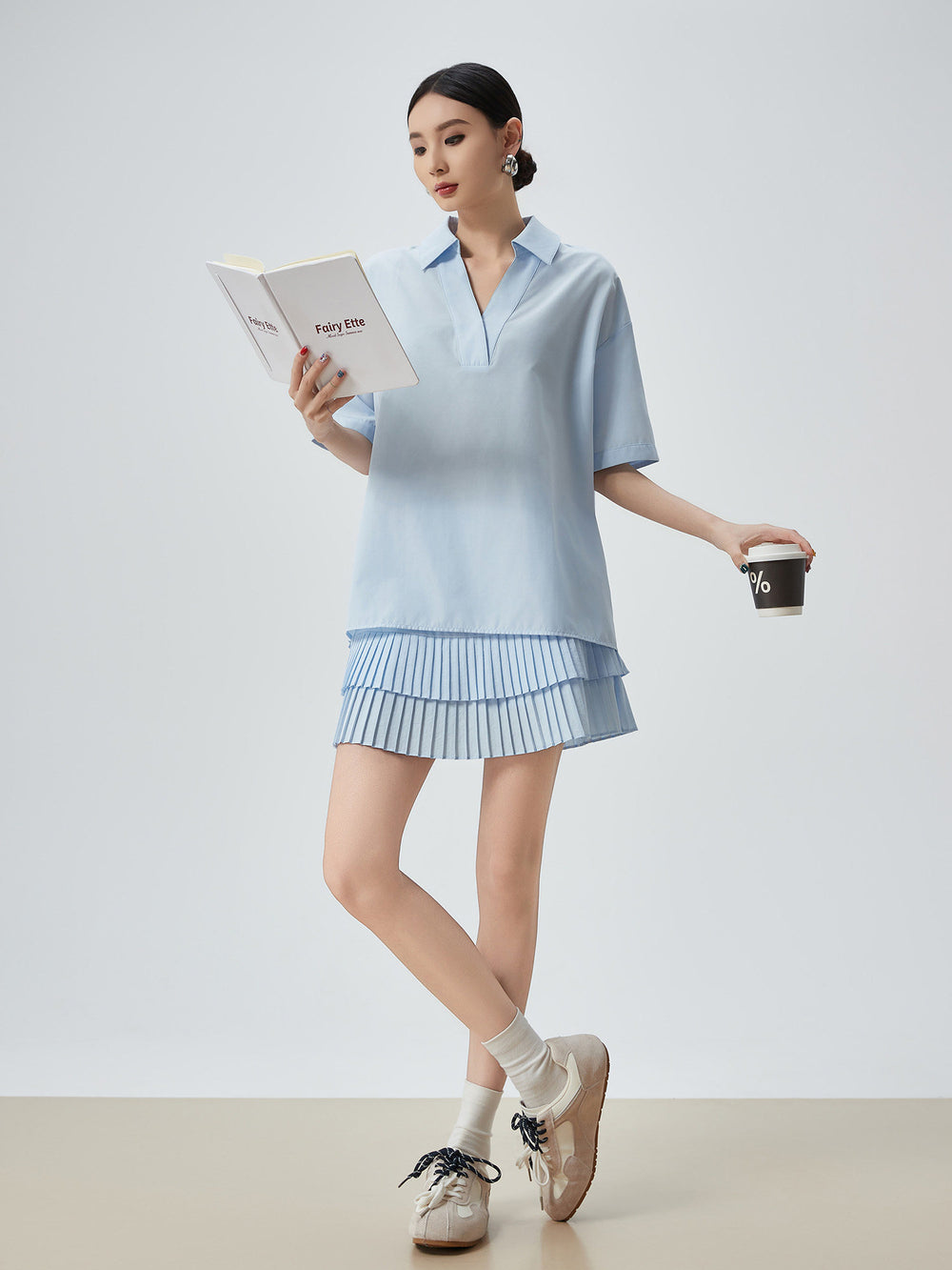Woman in light blue outfit holding a book and coffee cup on a plain background