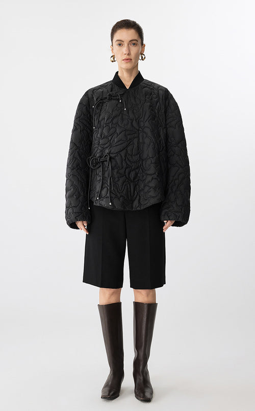 Person wearing a black quilted jacket, black shorts, and black knee-high boots on a white background