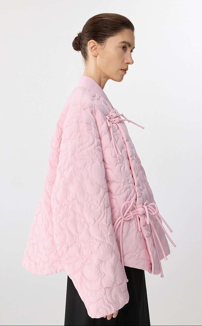 Woman wearing a pink quilted jacket with a white background