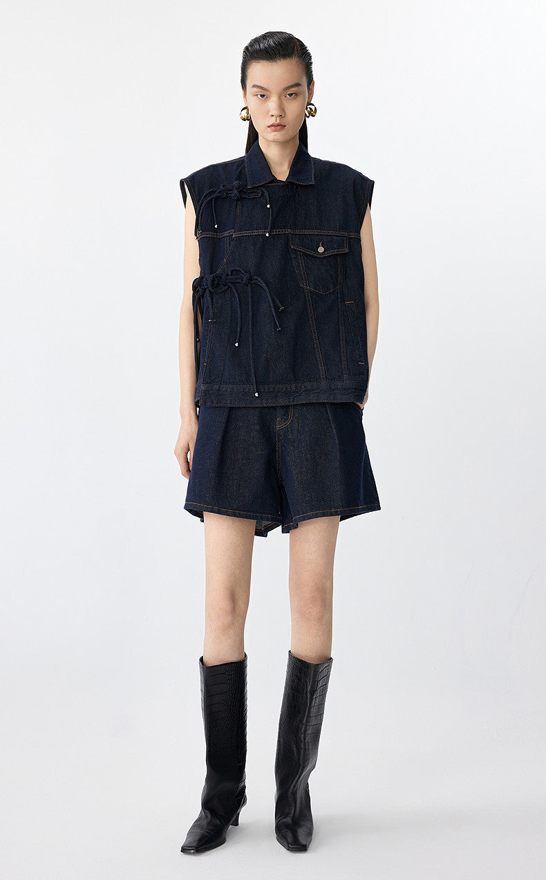 Person wearing a dark denim vest and skirt set with black knee-high boots on a white background