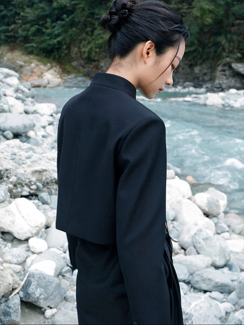 woman standing wearing a velvet suit jacket against a grey background. 