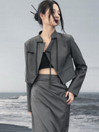 woman standing wearing a grey suit jacket against a grey background.  