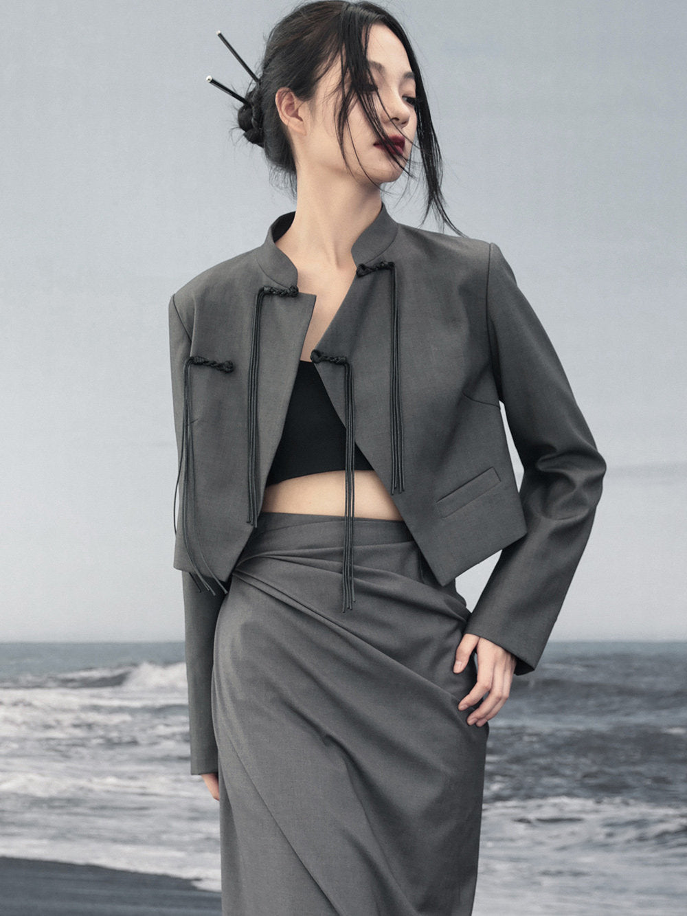 woman standing wearing a grey suit jacket against a grey background.  