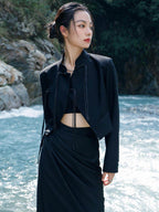 woman standing wearing a black suit jacket against a grey background.  