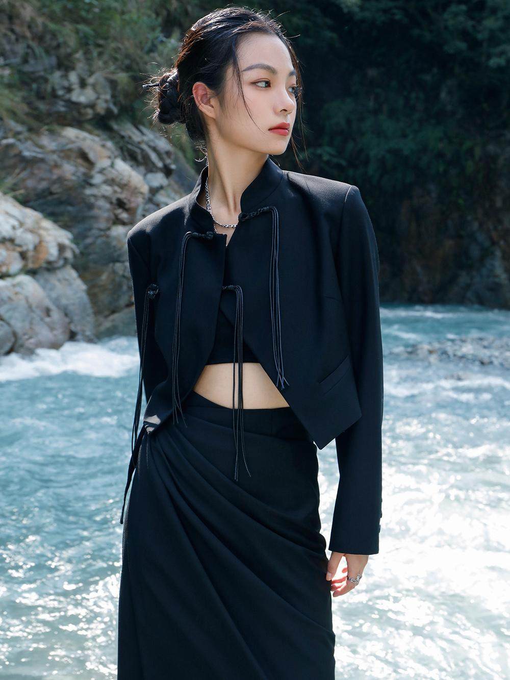 woman standing wearing a black suit jacket against a grey background.  