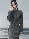 woman standing wearing a grey suit jacket against a grey background.  