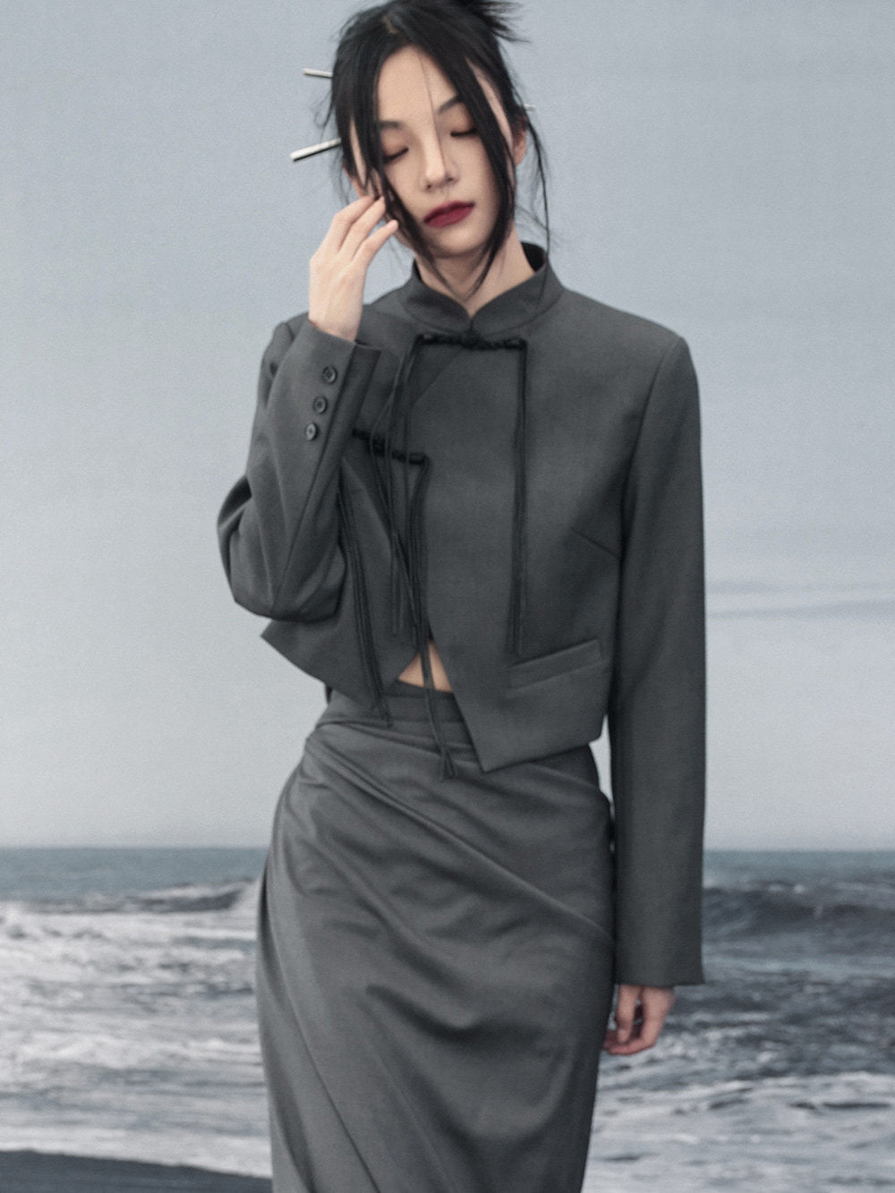 woman standing wearing a grey suit jacket against a grey background.  