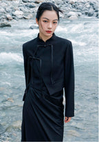 woman standing wearing a black suit jacket against a grey background. 