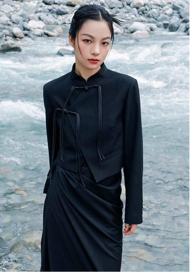 woman standing wearing a black suit jacket against a grey background. 