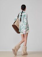 Woman wearing a patterned cardigan and beige boots, holding a brown bag on a plain background