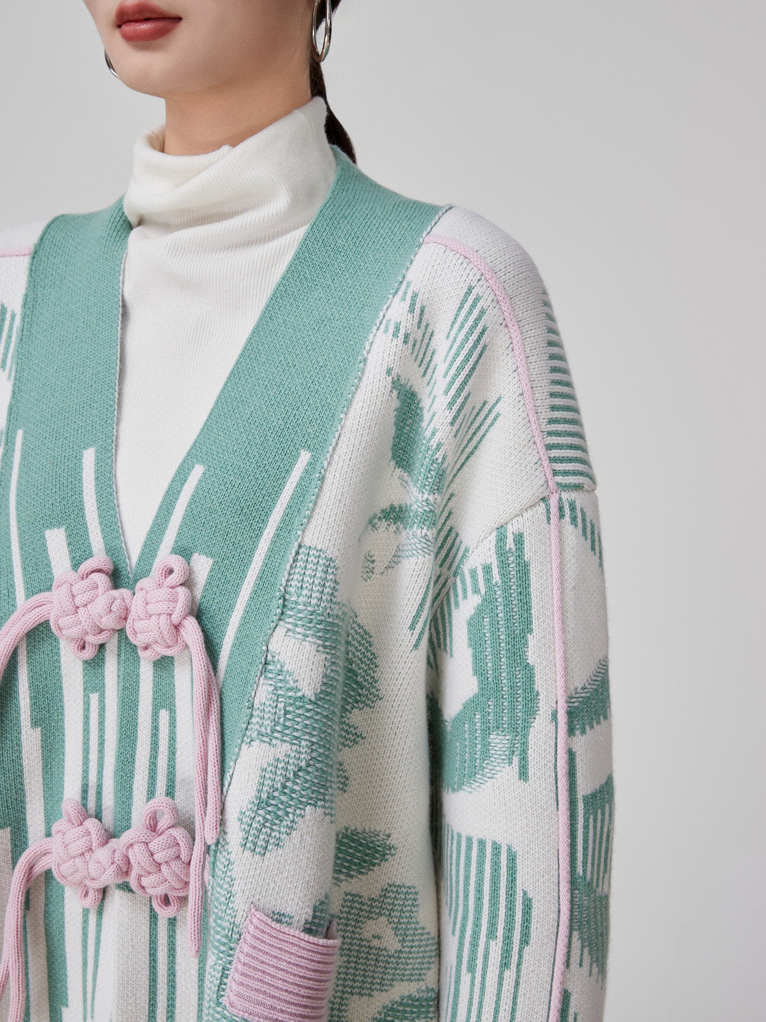 Person wearing a patterned cardigan with pink accents on a plain background