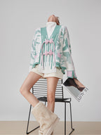 Person wearing a stylish outfit with a patterned cardigan and skirt, sitting on a chair.