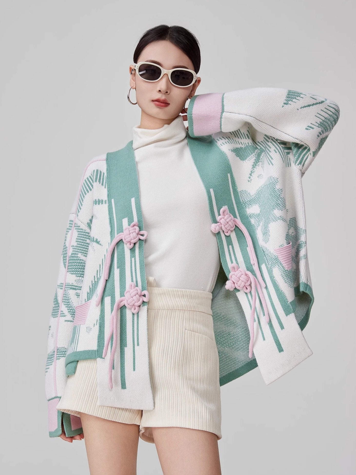 Person wearing a stylish outfit with a patterned cardigan on a plain background