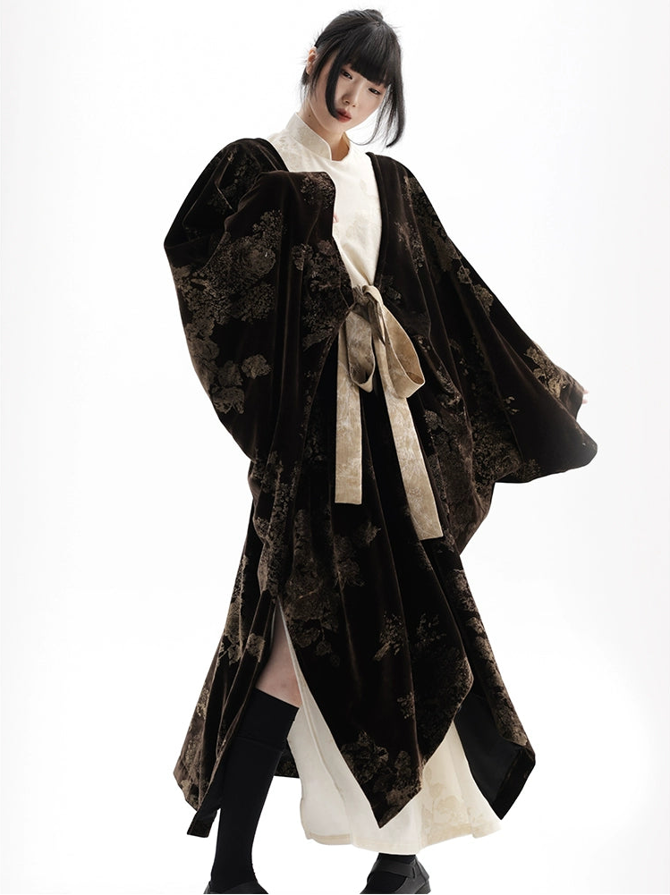 Person wearing a black floral patterned coat with a white shirt underneath on a white background