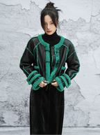 Person wearing a black jacket with green accents against a textured white wall.