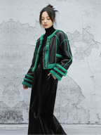 Person wearing a black and green jacket against a textured gray wall.