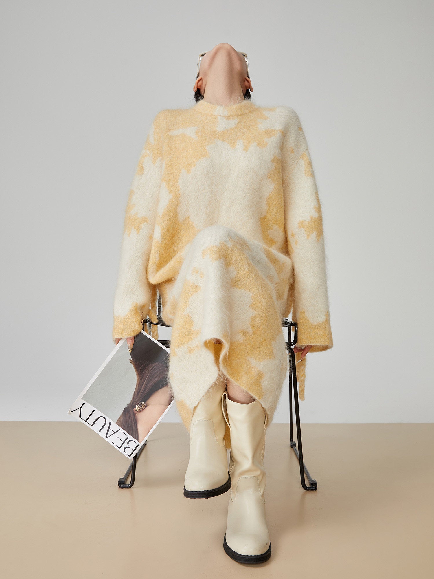 Person wearing a yellow and white tie-dye outfit with a magazine on a table.