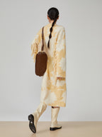 Person wearing a long, light-colored coat with a brown bag on a plain background