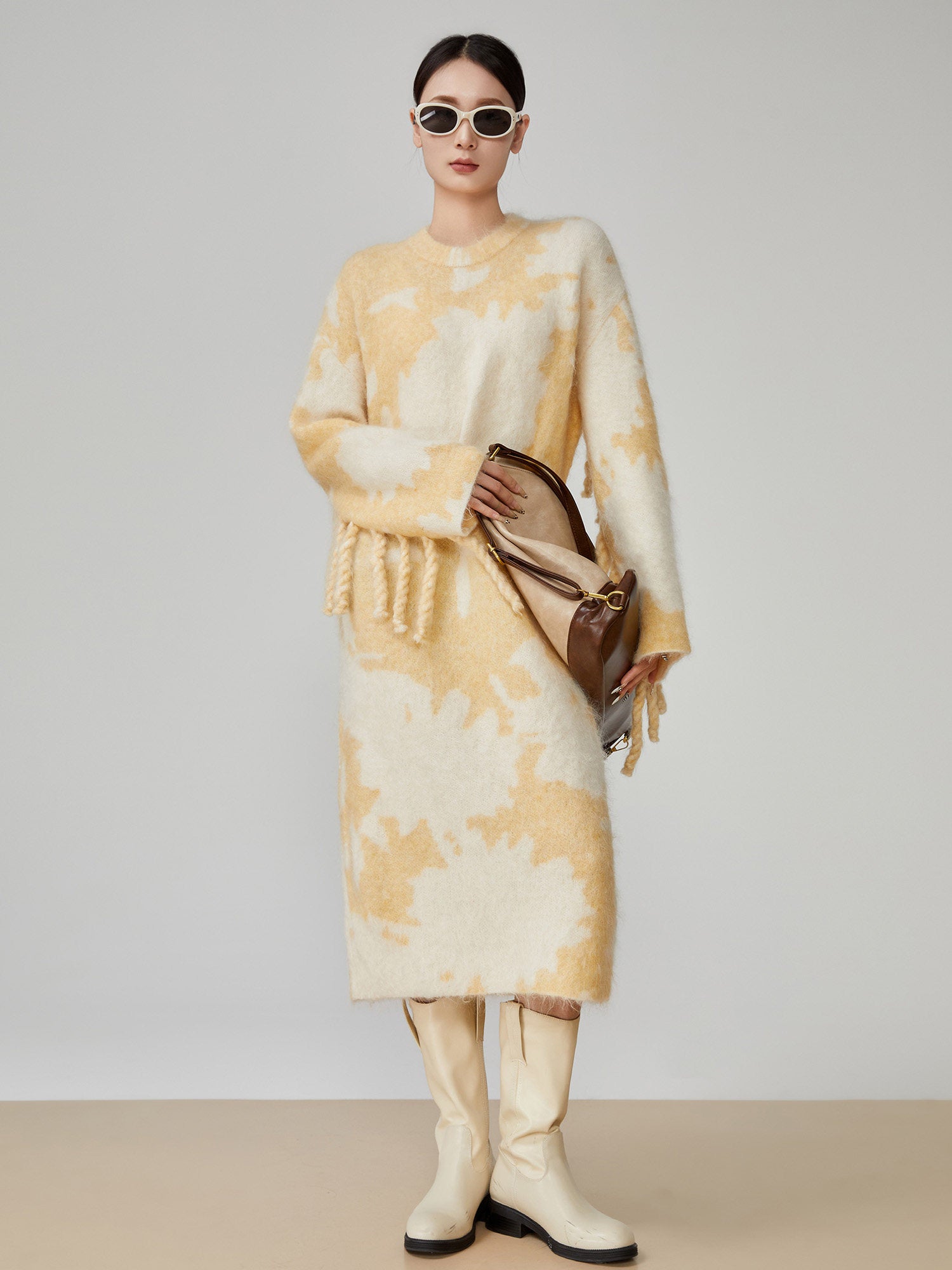 Woman wearing a yellow and white patterned outfit with a brown handbag on a plain background