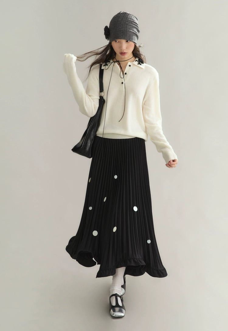 Woman wearing a white sweater and black pleated skirt with white polka dots on a plain background