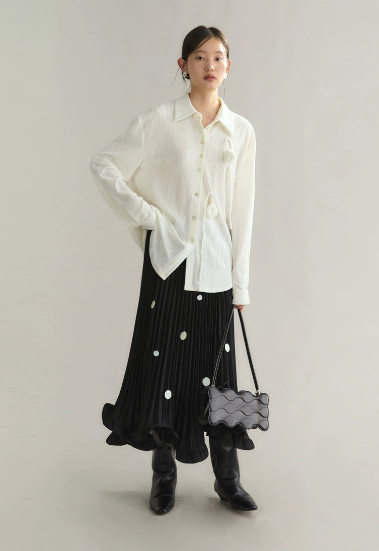 Woman wearing a white blouse, black pleated skirt, and black boots with a gray bag on a light gray background