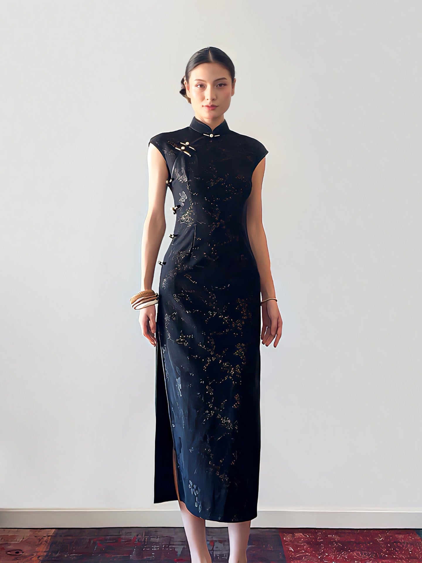 Woman wearing a black dress with gold patterns against a white wall.