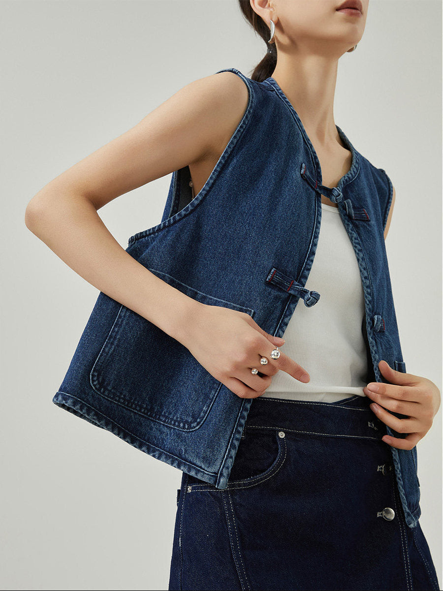 Person wearing a denim vest over a white top on a plain background