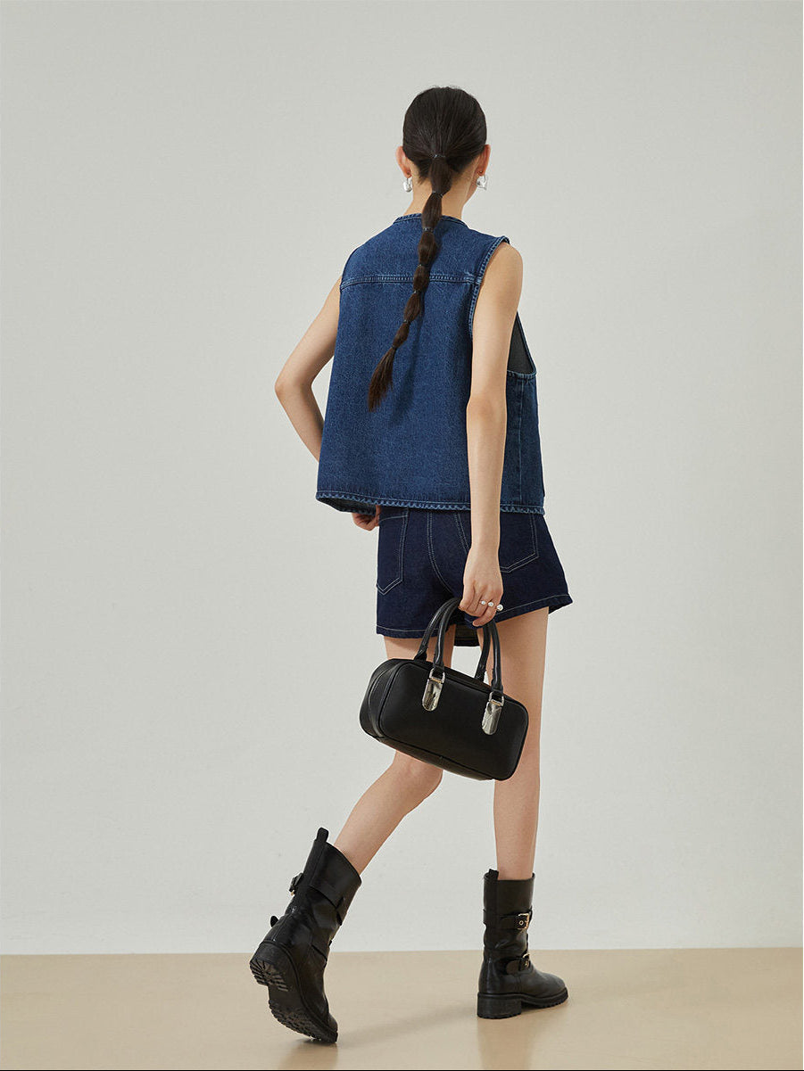 Woman wearing a denim outfit with a black handbag on a plain background