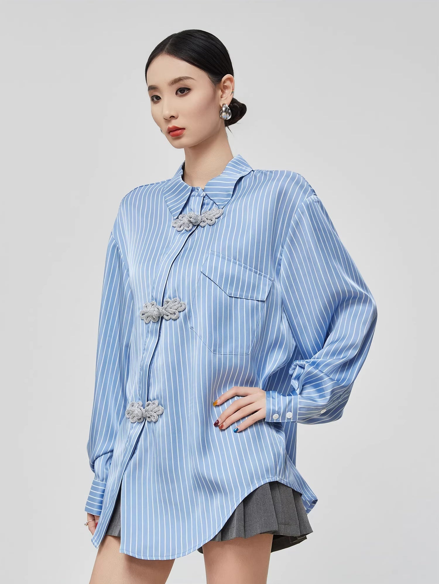 Woman wearing a blue striped shirt with decorative buttons on a gray background