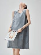 Woman wearing a denim dress holding a magazine against a plain background