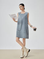 Woman wearing a denim dress holding a coffee cup and a book on a plain background