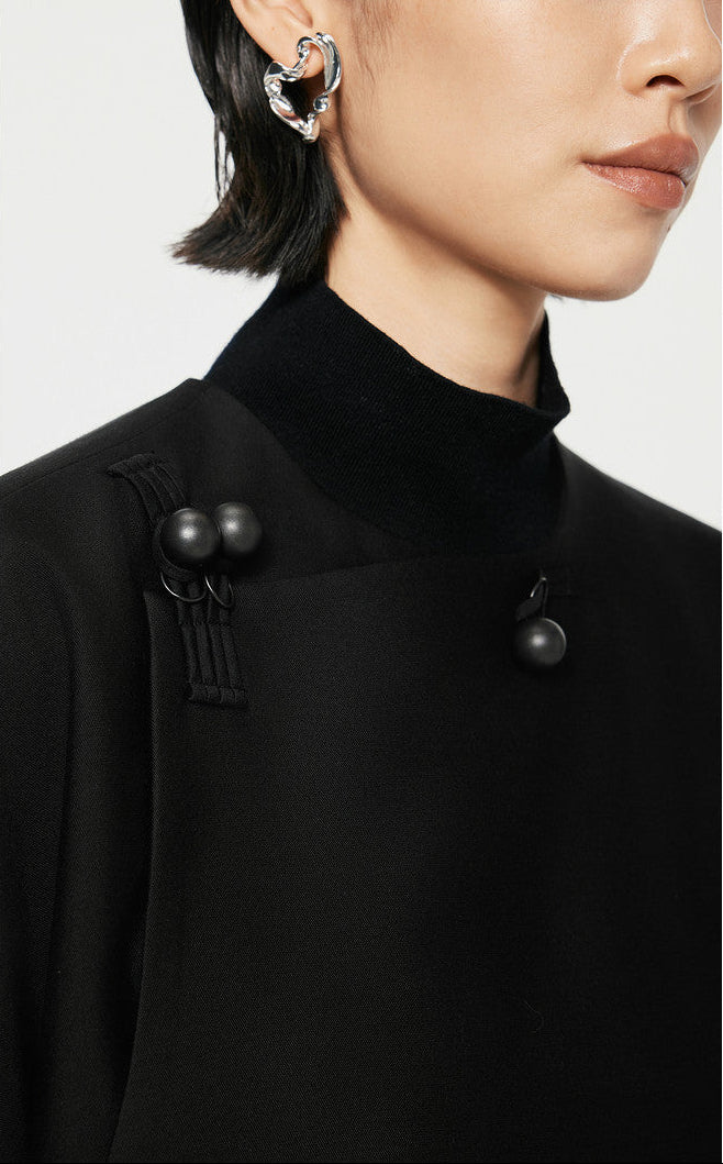 Close-up of a person wearing a black turtleneck with decorative buttons and earrings.