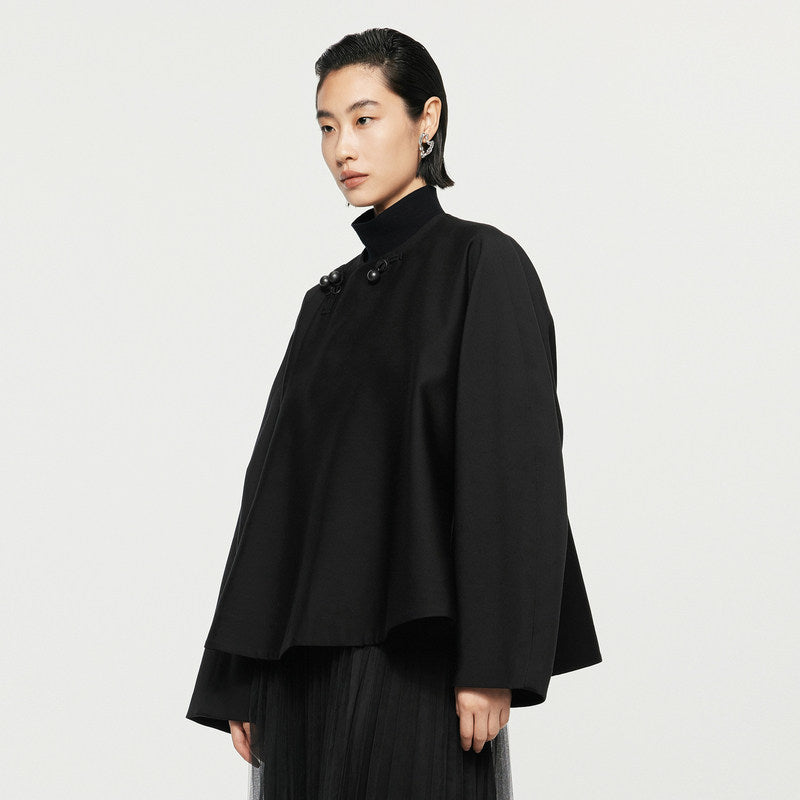 Person wearing a black coat against a plain background