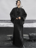 Person wearing a long black garment standing on a rocky beach.