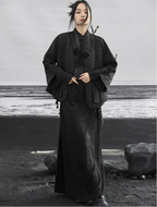 Person wearing a long black garment standing on a rocky beach.