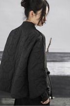 Person wearing a dark jacket with floral patterns, standing against a neutral background.